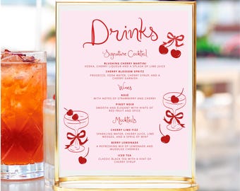 May include: A pink sign with a gold frame lists a drinks menu with a cherry motif. The menu includes signature cocktails, wines, mocktails, and iced tea. The text reads "Drinks Signature Cocktail, Blushing Cherry Martini, Cherry Blossom Spritz, Wines, Rose, Pinot Noir, Mocktails, Cherry Lime Fizz, Berry Lemonade, Iced Tea".