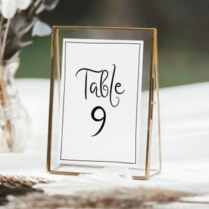 May include: A gold-toned metal frame with a white card inside. The card has black text that reads "Table 9".