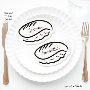 May include: Two sushi-shaped place cards, each with a name in cursive: "Jaimee" and "Samantha." They sit on white plates, with a gold fork and knife. The text "CHANGE TO ANY COLOR" is in the upper left corner. The cards are approximately 15 x 13 cm.