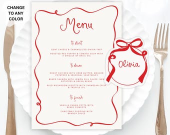May include: A red and white Christmas menu with a red ribbon ornament place card that says "Olivia". The menu lists a variety of dishes, including goat cheese and caramelized onion tart, roast chicken with herb butter, and vanilla panna cotta with berry compote.