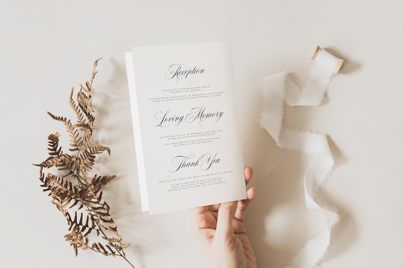 May include: A white folded card featuring black printed text with the headings Reception, Loving Memory, and Thank You. The card is displayed alongside a dried brown fern frond and a piece of white frayed ribbon on a neutral surface.