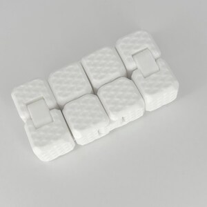 May include: White fidget toy made of interlocking squares with a textured surface. The toy is designed to be manipulated and flipped.