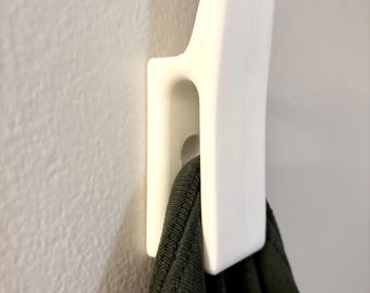May include: White plastic hook mounted on a wall with a dark green shirt hanging from it.