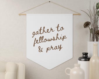 Puede incluir: Un cartel blanco con las palabras "gather to fellowship & pray" en escritura marrón. El cartel está suspendido de una varilla de madera y cuerda. Jarrones decorativos y una silla en el fondo.