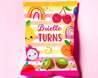 Peut inclure: Un sac de fête coloré avec un fond rayé rose et jaune. Il présente des illustrations de fruits souriants, des arcs-en-ciel et le texte "Brielle TURNS 5". Le sac est scellé en haut et a une base rose.