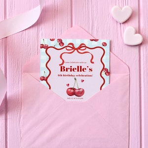 May include: A pink envelope with a white ribbon on a pink wooden background. The envelope contains a birthday invitation with a cherry theme. The invitation reads "Come Celebrate with us Brielle's 4th birthday celebration! July 27 at 3:00 pm".