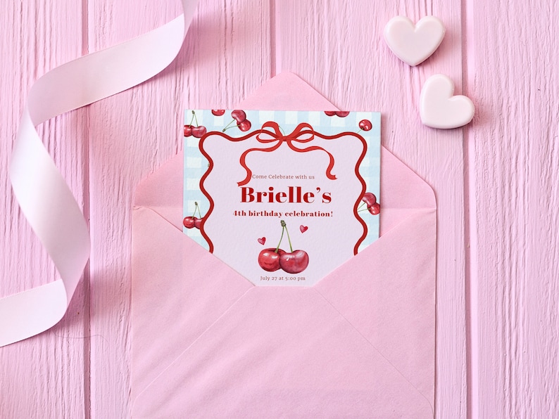 May include: A pink envelope with a white ribbon on a pink wooden background. The envelope contains a birthday invitation with a cherry theme. The invitation reads "Come Celebrate with us Brielle's 4th birthday celebration! July 27 at 3:00 pm".