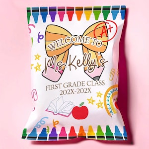 Op de afbeelding: Een witte zak met een kleurrijke krijtjesrand en de tekst "WELCOME TO Ms. Kelly's FIRST GRADE CLASS 202X-202X". De zak heeft illustraties van een strik, potlood, appel en open boek, met een A+ cijfer.