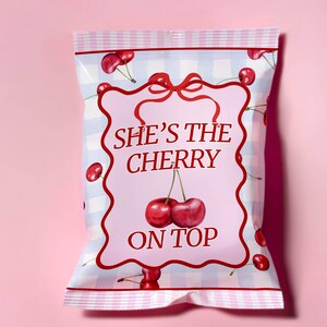 May include: A pink and white checkered bag with a pink label that says "She's the cherry on top" with a red bow and cherries on the bag.