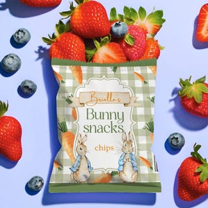 Könnte beinhalten: Eine Tüte "Brielle's Bunny Snacks Chips" mit grün-weißem Karomuster, Karotten und Kaninchenillustrationen. Die Tüte ist gefüllt mit Erdbeeren, Blaubeeren und Himbeeren auf hellblauem Hintergrund.
