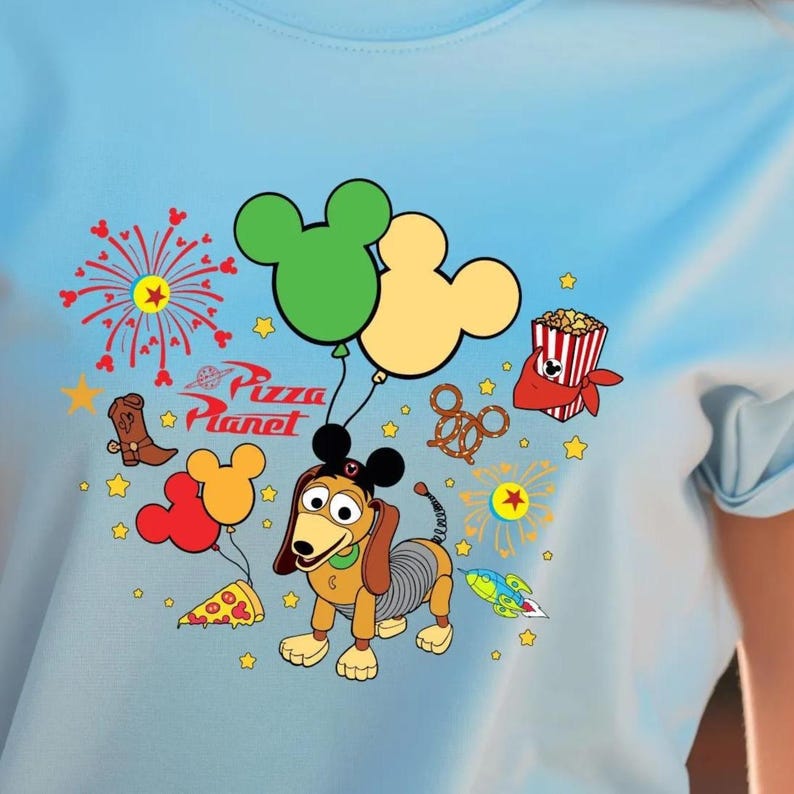 A t-shirt with a colorful graphic design featuring various Disney characters and elements, such as Mickey Mouse, fireworks, popcorn, and a dog.
