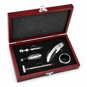 Puede incluir: Un juego de accesorios para vino en una caja rectangular de madera oscura con cierre de metal plateado. El set incluye un tapón de botella de metal plateado con cabeza esférica, un vertedor, un sacacorchos, un anillo antigoteo y un termómetro.