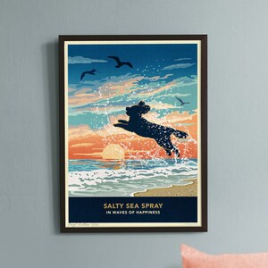May include: A framed print titled "Salty Sea Spray" shows a black dog jumping in the sea at sunset. The artwork uses blue, orange, and white. A sleeping dog rests on a grey surface below the artwork. The text reads "in waves of happiness".