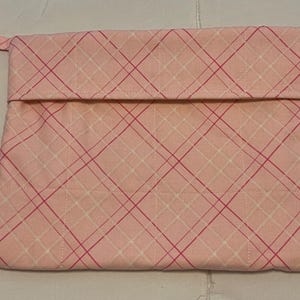 Può includere: Un astuccio in tessuto trapuntato rosa con chiusura a patta e un piccolo passante. La pochette presenta un motivo a quadri nei toni del rosa e del bianco. Il tessuto è cucito con un motivo a griglia.