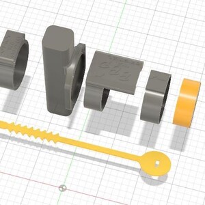 Peut inclure: Vue éclatée d'un ensemble de composants en plastique gris, comprenant plusieurs pièces en forme d'anneau, une pièce rectangulaire avec du texte et un corps central rectangulaire. Un ruban orange et une attache jaune dentée sont également inclus. Les composants sont disposés sur une grille.