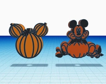 May include: Two decorative ornaments featuring orange and black designs. One is a pumpkin shaped like a mouse head with rounded ears. The other depicts a black mouse character sitting on top of a large orange pumpkin with carved details.
