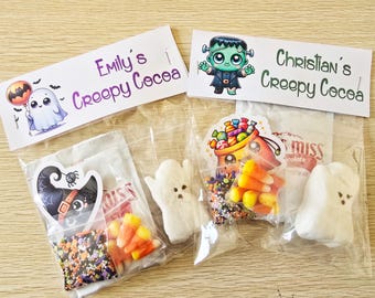 May include: Two clear cellophane bags filled with Halloween treats. One bag has a sticker of a black cat in a witch hat, candy corn, and sprinkles. The other bag has a Frankenstein sticker, candy corn, and a marshmallow ghost. The text "Emily's Creepy Cocoa" and "Christian's Creepy Cocoa" are on the top.