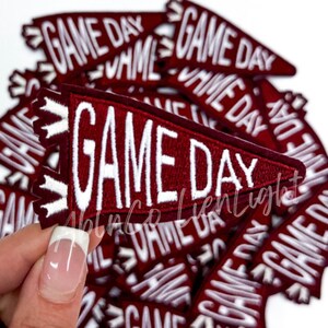 May include: A pile of maroon felt pennant patches with white embroidered text that reads "GAME DAY".