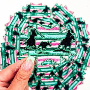 May include: A close-up of a stack of green and pink striped iron-on patches featuring a silhouette of a person riding a horse. The patches are in the shape of a star.