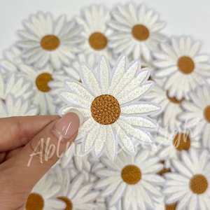 May include: A collection of white felt daisy flower iron-on patches with a brown center.