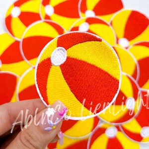 May include: Embroidered patches featuring a beach ball design in red, yellow, and white. The patches are round and have a stitched border. The image shows a collection of these patches, with one held up in front of the others.