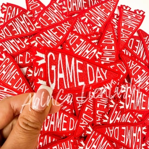 May include: A pile of red felt pennants with white embroidered text that reads "GAME DAY".