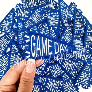 May include: A pile of blue felt pennant patches with white embroidered text that reads "GAME DAY".