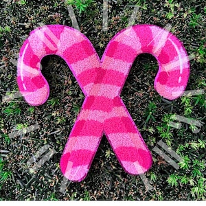 May include: A pink and white striped candy cane ornament with a fuzzy texture. The ornament is shaped like a candy cane and is perfect for decorating a Christmas tree.
