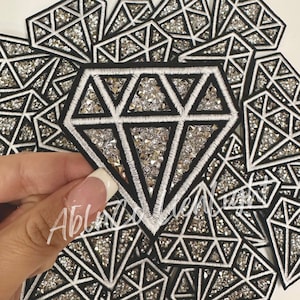May include: A pile of black and white diamond-shaped patches with silver glitter. The patches are sewn with white thread and have a black outline.