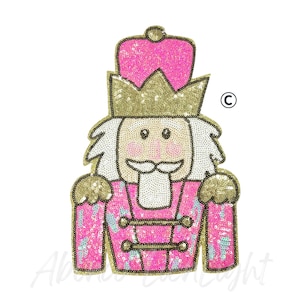 May include: A pink sequined Nutcracker soldier with a gold crown and accents. The design features a white beard and mustache, and a pink jacket with gold buttons. The image is on a white background.