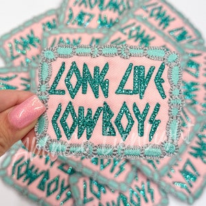 May include: A pink fabric patch with a turquoise border and turquoise rhinestones spelling out "Long Live Cowboys".