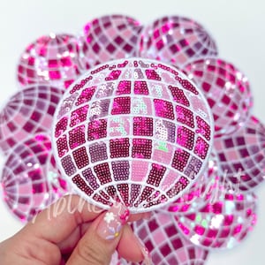 May include: A pink and white sequin disco ball patch. The patch is round and has a white outline. It is surrounded by other smaller pink and white sequin disco ball patches.