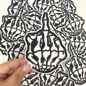 May include: A set of 12 iron-on patches featuring a skeleton middle finger in a black and white design. The patches are approximately 3 inches in diameter.