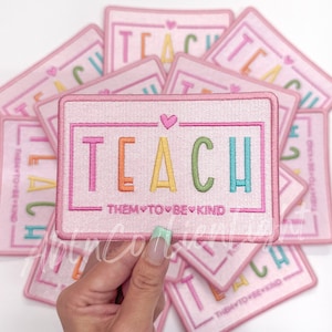 May include: A stack of pink iron-on patches with the word "TEACH" in rainbow colors and the text "them to be kind" in a smaller font.