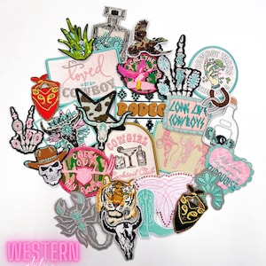 May include: A collection of colorful iron-on patches with western themes. The patches feature images of a skull, a tiger, a scorpion, a cowboy boot, a cow skull, a cactus, a tequila bottle, a martini glass, a horseshoe, a peace sign, a bandana, and more. The patches have text that says "Loved by a Cowboy", "Rodeo", "Long Live Cowboys", "Cowboy Tears", "Check Out My Rack", "Cowgirl Cocktail Club", and "Turquoise".