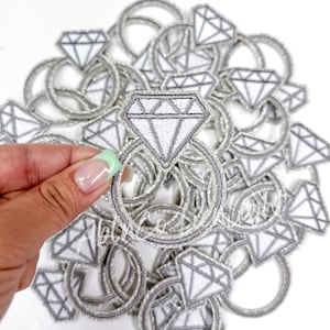 May include: A pile of silver glitter iron-on patches featuring a diamond ring design.