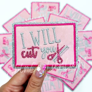 May include: A pink and silver embroidered patch with the text "I WILL cut you" and a pair of pink scissors and a silver comb.