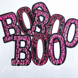 May include: Pink and black fabric letters spelling "BOO" with a spiderweb design. The letters are made of sequins and are perfect for Halloween decorations.