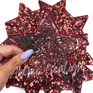 May include: A set of six burgundy star-shaped patches with sequins. The patches are approximately 3 inches in diameter.