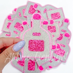 May include: A stack of pink and gray felt patches shaped like bottles with glitter accents. The patches are perfect for adding a touch of sparkle to any project.