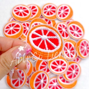 May include: A pile of orange and red embroidered iron-on patches shaped like a slice of grapefruit.