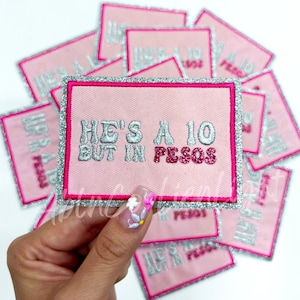 May include: Pink fabric patch with silver glitter trim. The patch has the text "He's a 10 but in pesos" in silver and pink glitter lettering.