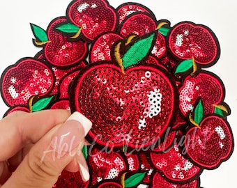 May include: A group of red sequin apple iron-on patches. The patches are all the same size and shape, and they have a green stem and leaf. The patches are perfect for adding a touch of whimsy to clothing, bags, or other accessories.