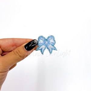 May include: A light blue glitter bow with a white outline. The bow is a decorative embellishment for crafts and clothing.