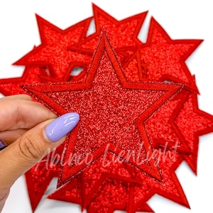 May include: A pile of red glitter star-shaped iron-on patches. The stars have a slightly raised outline.