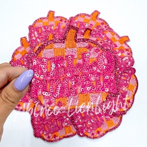 May include: A stack of pink and orange iron-on patches with the text "Hello Autumn" in pink sequins. The patches have a checkered pattern.
