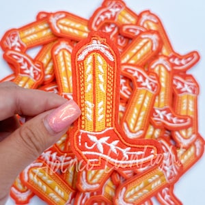 May include: A pile of orange and white felt cowboy boot patches. The patches are embroidered with a white stitching design.