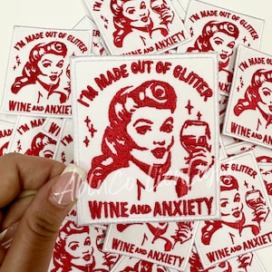 May include: White iron-on patch with red embroidery. The patch features a cartoon woman with red hair and a glass of wine. The text on the patch reads "I'm made out of glitter, wine and anxiety."