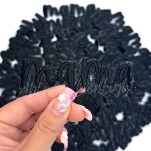 May include: Black glitter iron-on patch with the word "mama" in a cursive font.