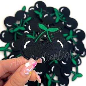 May include: A pile of black and green cherry patches. The cherries are embroidered with white stitching. The patches are about 1 inch in diameter.